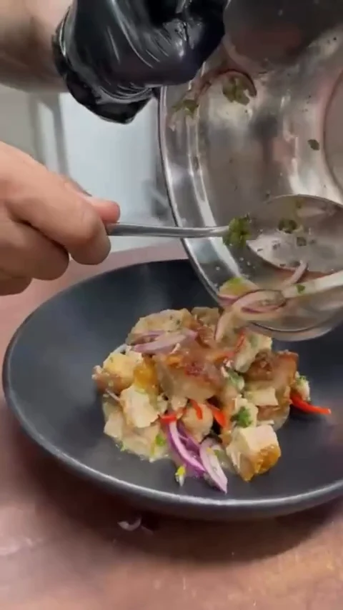 Ceviche de chicharrón: se vierte el líquido sobre trozos crujientes con cebolla morada en un bowl negro