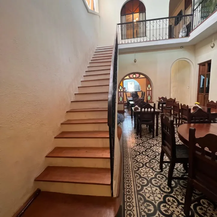 Comedor de la casa: mesas de madera sobre piso de mosaico, junto a la escalera del patio